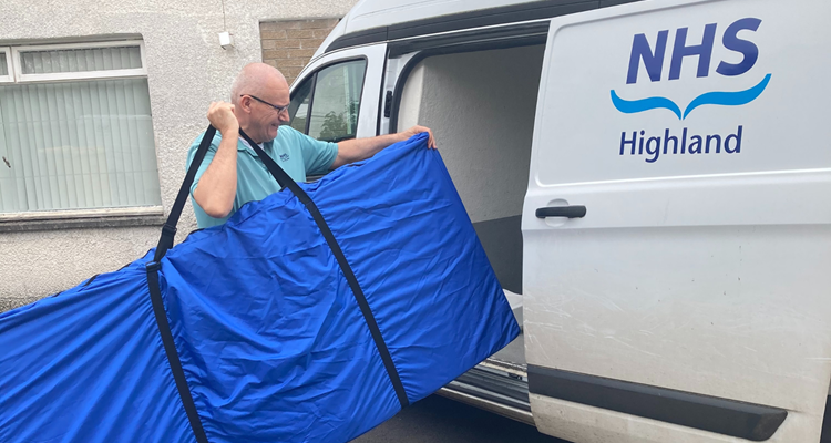 NHS employee carrying a rectangular large bag into an NHS van