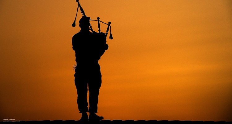 silhouette of a Highland Piper from the Armed Forces against an orange sky