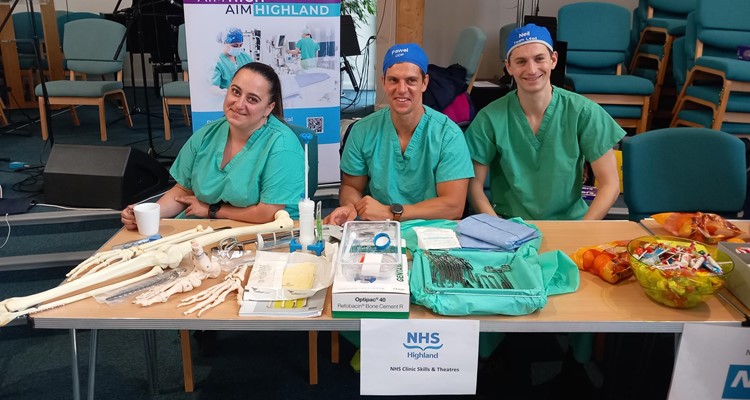 3 NHS Highland staff in gowns at a display table