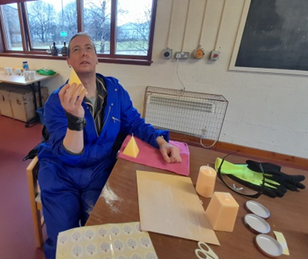 A supported person in blue overalls proudly holding their hand-made candle. 