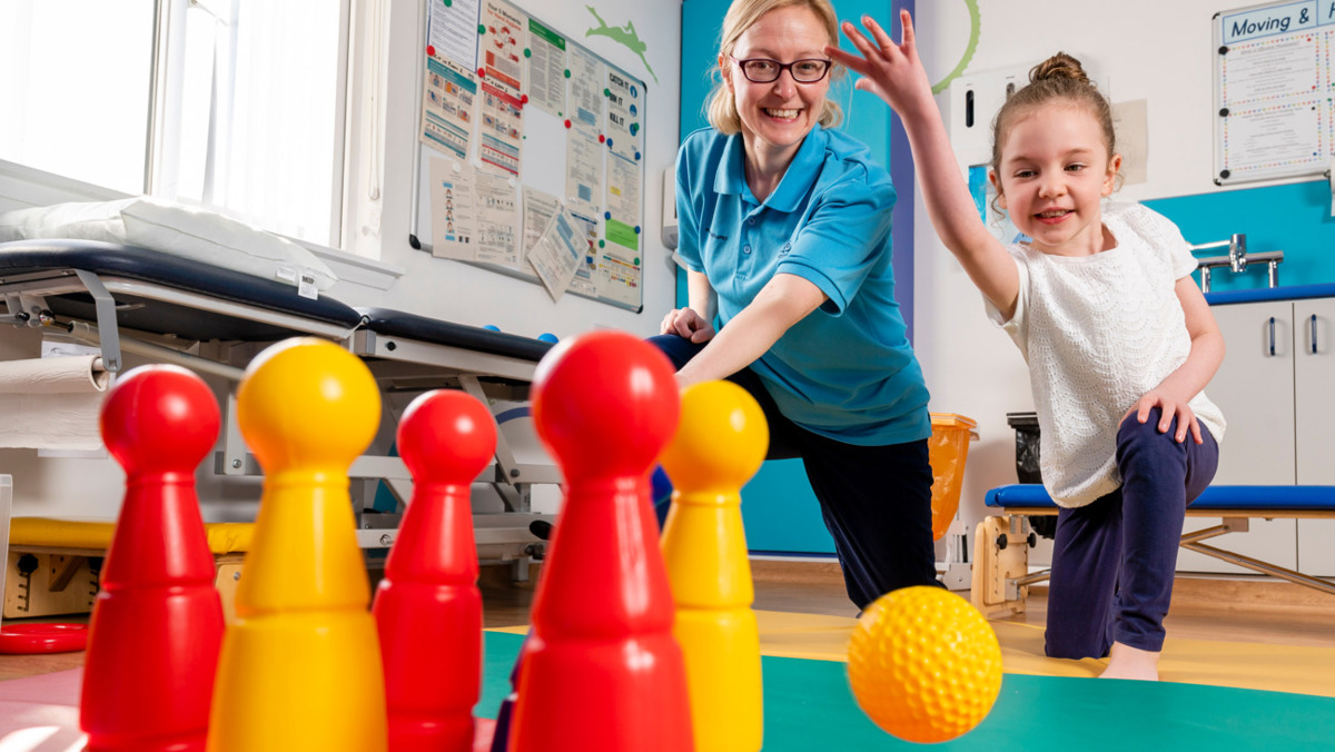 Physiotherapist With Child Playing Skittles