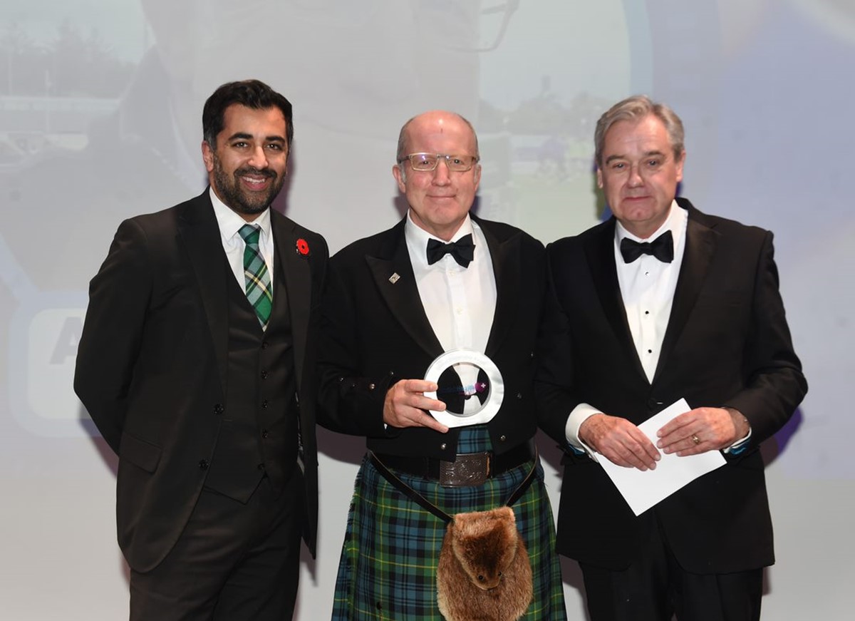 Mr. Kent, 58 years old, holds his trophy stood between Humza Yousaf MSP, Cabinet Secretary for Health and Social Care and another older man.