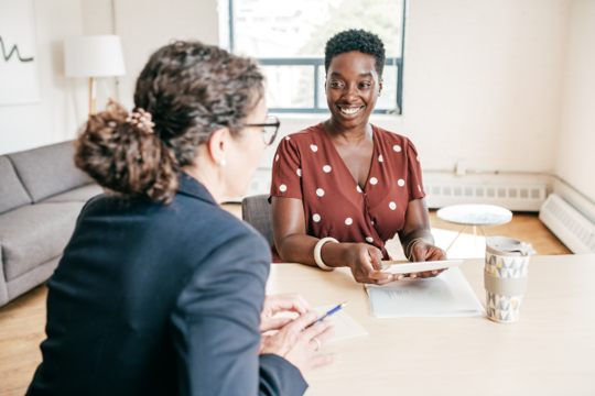 Two Women Talking And Smiling At A Desk