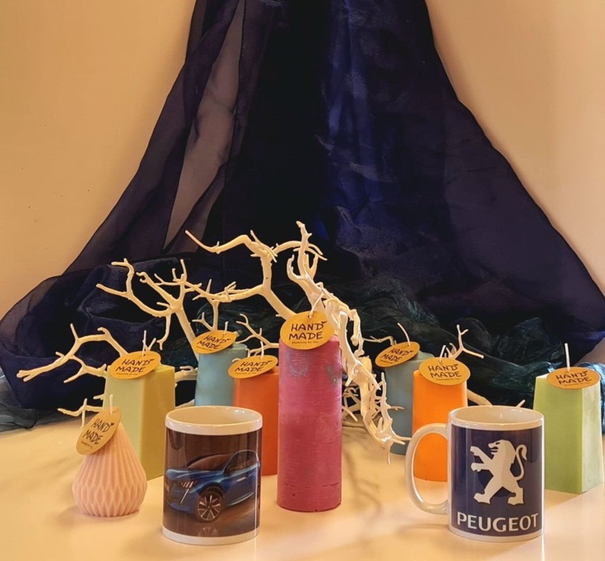 An array of brightly coloured, hand-crafted candles on a table in front of a navy blue velvet curtain