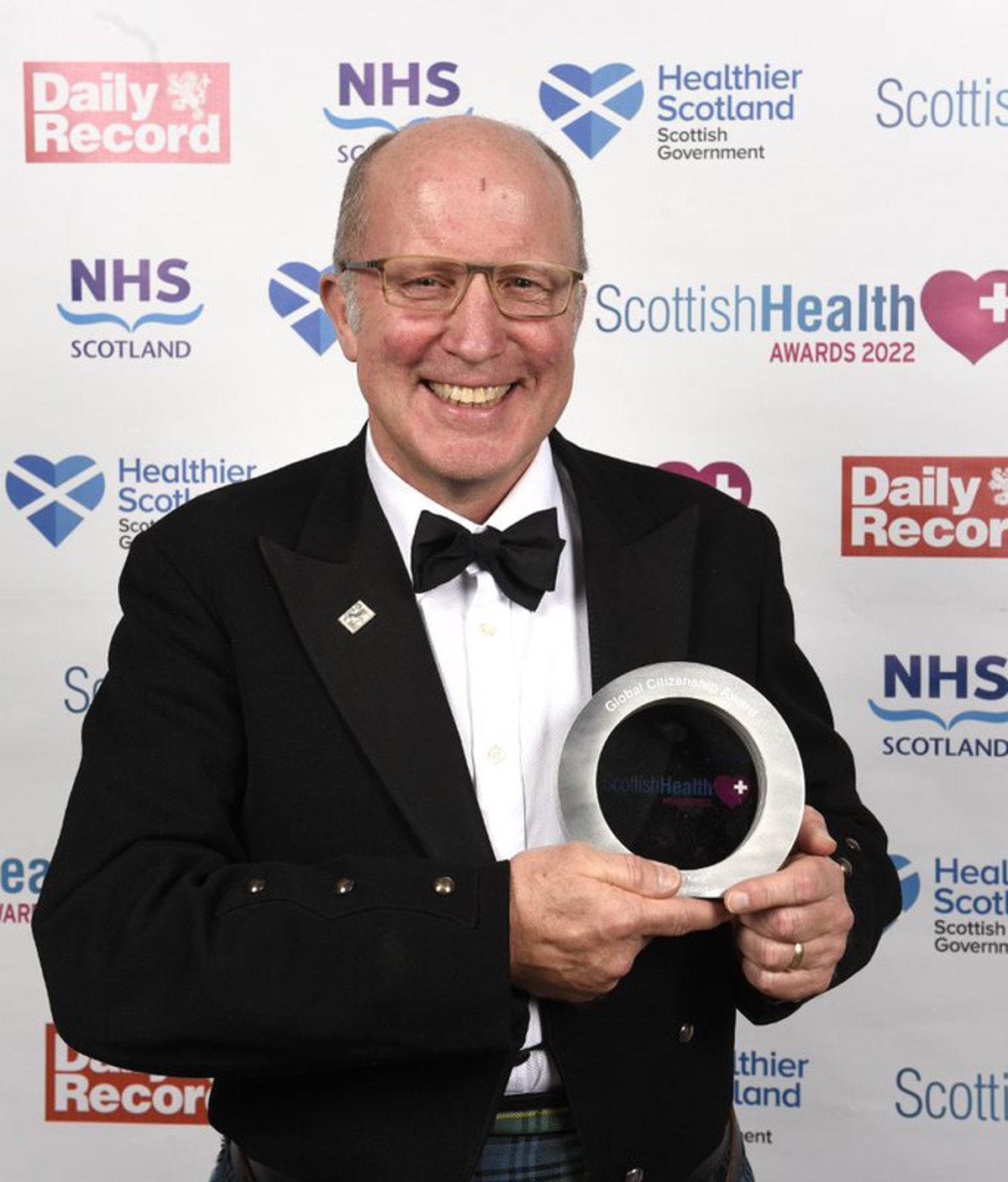  Mr. Andrew Kent, 58 years old, proudly holds his trophy donned in a suit jacket, shirt, bow tie and kilt.